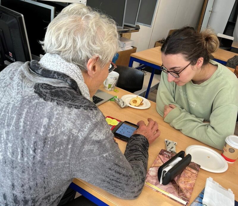 Eine junge Frau und eine ältere Person an einem Tisch, in dessen Mitte ein Handy liegt