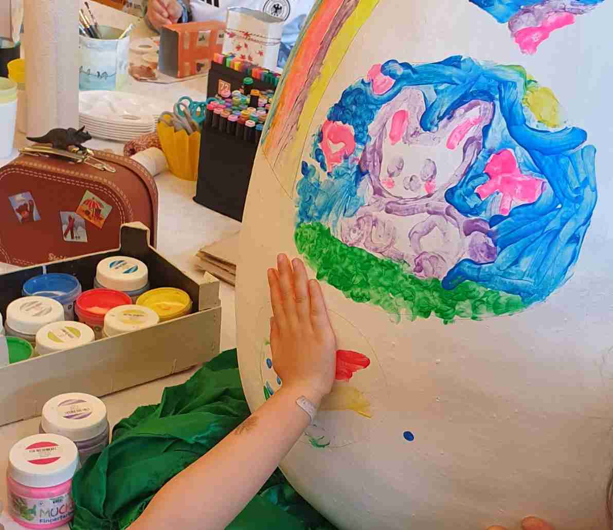 Eine Kinderhand bedruckt ein Osterei aus Pappmaché mit bunten Farben.